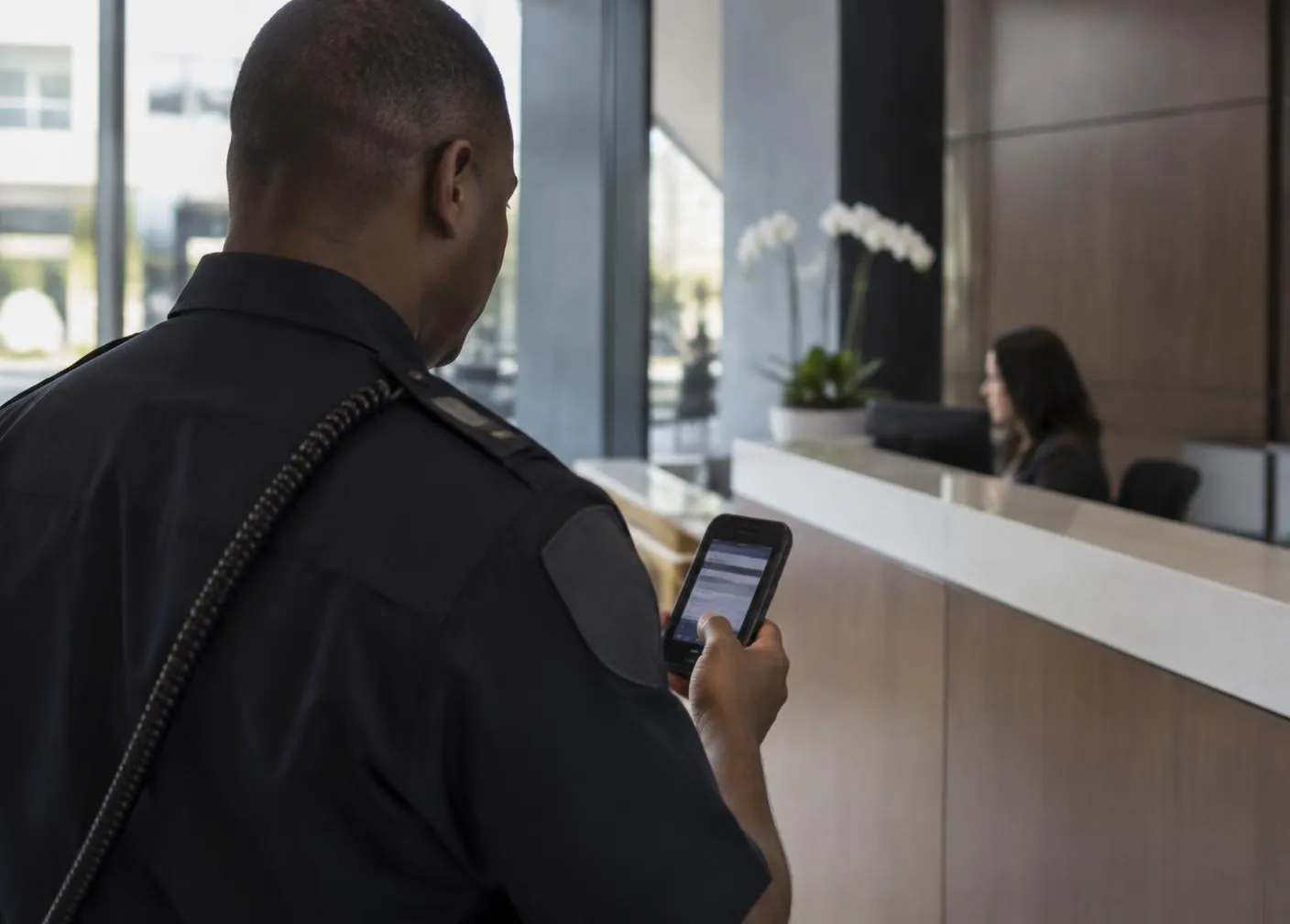 Security officer checking a mobile device in a building lobby beside the reception desk